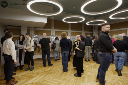 Uczestnicy oglądają obrazy. W środku stoi kobieta w czarnej koszuli z krótkim rękawem. Rozmawia z dwoma innymi kobietami.