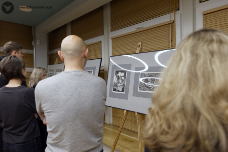 Mężczyzna w szarej bluzie ogląda dwa obrazy na sztaludze. Jeden z nich przedstawia Wieże Trynitarską w Lublinie.