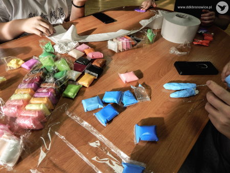 Na stole warsztatowym leża kolorowe elementy potrzebne do skonstruowania dłoni. Są w kolorze niebieskim, zielonym żółtym, brązowym.