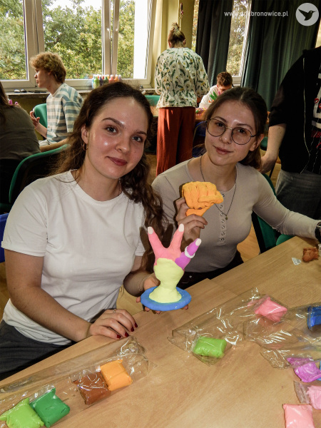 Dwie uczestniczki wymiany pokazują małe kolorowe rzeźby. Przedstawiają małe dłonie. Jedna dłoń jest koloru pomarańczowego. Druga fioletowo-różowa.