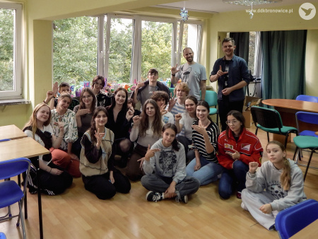 Uczestnicy wymiany pozują do grupowego zdjęcia. Większość z nich siedzi na podłodze. Stoi Łukasz Drozd, kierownik programowy. Wszyscy są uśmiechnięci.