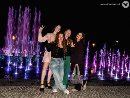 Cztery uczestniczki wymiany pozują do zdjęcia. Za nimi rozświetlona na fioletowo fontanna na Placu Litewskim.