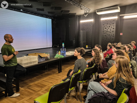 Sala teatralna. Po lewej stronie stoi kierownik programowy Łukasz Drozd. Przemawia do uczestników wymiany. Siedzą oni po prawej stronie.