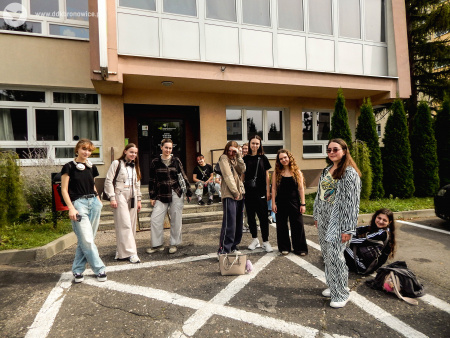 Grupa uczestniczek stoi przed Pracowniami Kultury Maki. Za nimi, na schodach siedzą dwie dziewczyny.