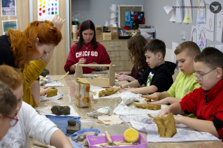 Pracownie Kultury Dziesiąta. Stół warsztatowy. Dzieci po obu stronach stołu siedzą i pracują nad ozdobą rękodzielniczą.