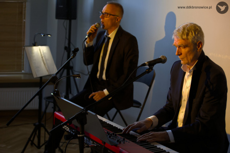 Patrycjusz Sokołowski i Gabriel Menet rozpoczynają koncert. Po prawej stronie Gabreil Menet w garniturze gra na czerwonym pianinie. Patrycjusz Sokołowski siedzi po lewej stronie w garniturze. Śpiewa do mikrofonu.