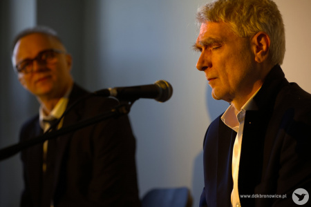 Artyści oświetleni żółtym światłem. Po prawej stronie Gabriel Menet. Ma zamknięte oczy. Skupia się na muzyce. W tle wokalista patrzy na pianistę.