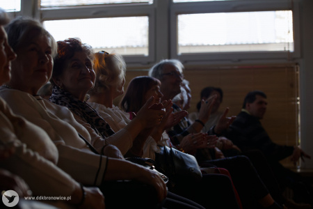 Pierwszy rząd widowni. Osoby klaszczą i uśmiechają się. W tle duże okna.