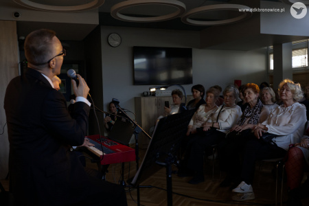 Inna perspektywa. Zza pleców artystów widać widownię. Patrycjusz Sokołowski śpiewa do mikrofonu. W tle widać zawieszony czarny telewizor na ścianie.