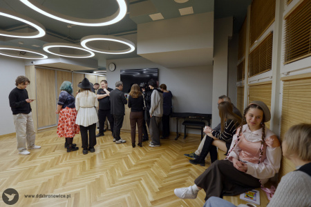 Uczestnicy wystawy rozmawiają w holu. Osoby po prawej stronie siedzą na parapecie.