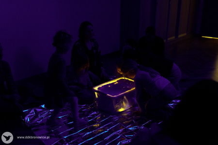 W pomieszczeniu delikatne niebieskie światło. Jest prawie ciemno. Na środku pomieszczenia pudełko. Z pudełka wychodzi żółte światło.