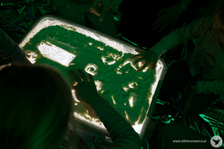 Podświetlone pudełko. Na wierzchu pudełka sypki piasek. Dzieci rysują wzory palcami na wierchu pudełka.