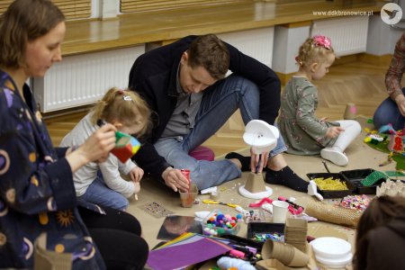 Tata pomaga swojej córce w tworzeniu kolorowej ozdoby. Obok nich na podłodze siedzi Agata Pawłowska.