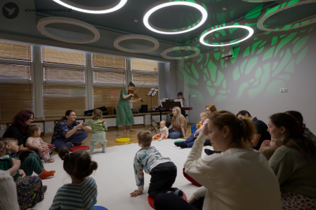 Uczestnicy słuchają muzyki skrzypiec. Siedzą na białym dywanie. W tle, Sylwia Namroży gra na skrzypcach. Dzieci wchodzą na biały dywan.