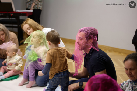 Mężczyzna ma założoną różową chustę. W tle dziewczynka ma założoną zieloną chustę.