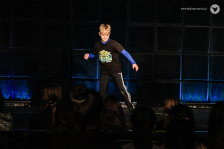 Na scenie niebieskie światło. Na środku sceny tańczący chłopak. Ma czarno-niebieską bluzę i dresy.