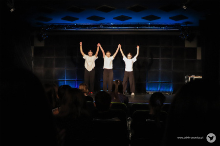 Trzy dziewczyny w białych koszulkach stoją na scenie. Trzymają się za ręce, mają je uniesione wysoko w górze.