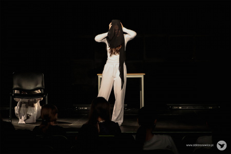 Aktorka w białym stroju na głowie ma założony czarny materiał.