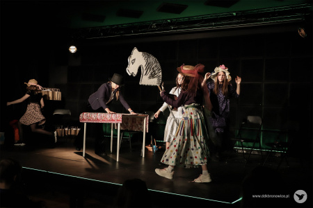 Dziewczynka w jasnej spódnicy w kolorowe groszki przemieszcza się po scenie. Trzyma w ręce kij na którym umieszczona jest styropianowa głowa konia.