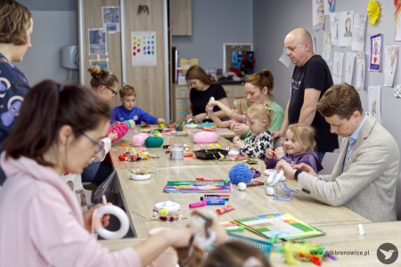 Uczestnicy tworzą świąteczne ozdoby. Po prawej stronie widać dwóch mężczyzn pomagających swoim dzieciom.
