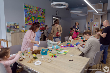 Uczestnicy tworzą ozdoby przy długim stole. W tle po prawej stronie widać kierowniczkę Pracowni Kultury Dziesiąta, Agatę Pawłowską.