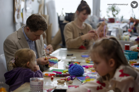 Mężczyzna w jasnej marynarce i błękitnej koszuli pomaga córce w stworzeniu artystycznej i kolorowej ozdoby.