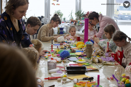 Uczestnicy pracują nad swoimi ozdobami. Siedzą przy stole. Na stole rozłożone kolorowe materiały.