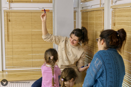 Mama siedzi na parapecie i uśmiecha się do dziewczynki. Trzyma wysoko w ręce fragment ozdoby.
