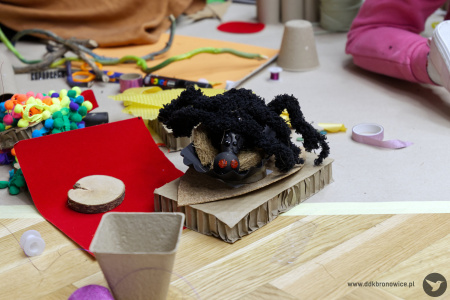 Na tekturce duży czarny pluszowy pająk. Ma czerwone oczy.