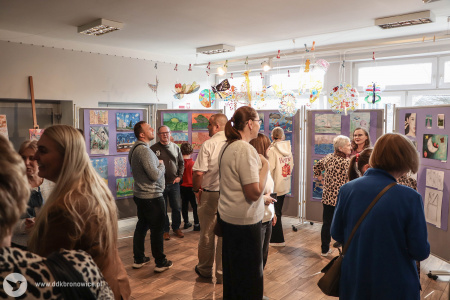 Dorośli rozmawiają o obrazach. Wokół nich rozwieszone obrazy malowane przez dzieci.