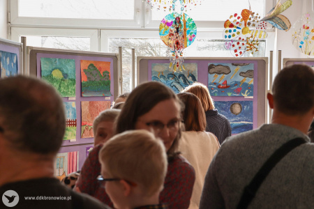 Dorośli oglądają wystawę. Z sufitu zwisają kolorowe ozdoby przedstawiające owady.