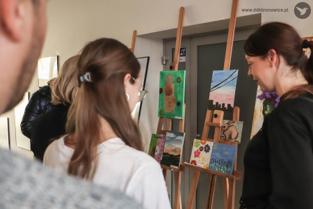 Uczestnicy oglądają mniejsze obrazy zawieszone na sztalugach.
