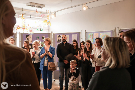 Osoby obecne na wystawie klaszczą w dłonie. Uśmiechają się.