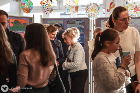 Rodzice z dziećmi oglądają wystawę w Galerii Małej. W tle widać obrazy zawieszone na fioletowych tłach.