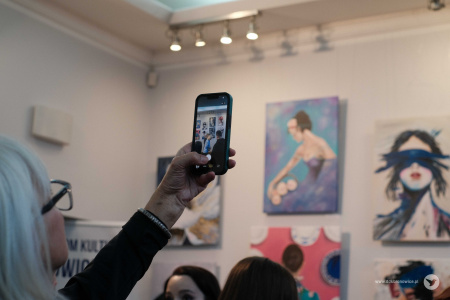 Kobieta ubrana w czarną bluzkę robi zdjęcie telefonem wiszącym obrazom.