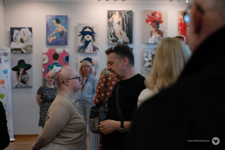 Mężczyzna w czarnym swetrze rozmawia z dziewczynką ubraną w szarą bluzkę. Stoją profilem.