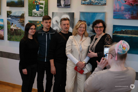 Trzy kobiety i dwóch mężczyzn ustawia się do zdjęcia. Zdjęcie robi telefonem dziewczynka w szarej bluzce.