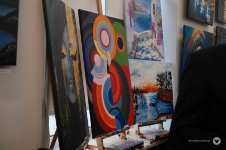 Obrazy wiszące na wystawie. Jeden z nich przedstawia kolorowe kręgi i półkręgi. Każdy z nich w innym kolorze. Razem tworzą zamkniętą strukturę.