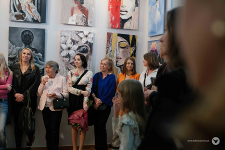 Uczestnicy grupy MalujeMY stoją na tle zawieszonych obrazów.