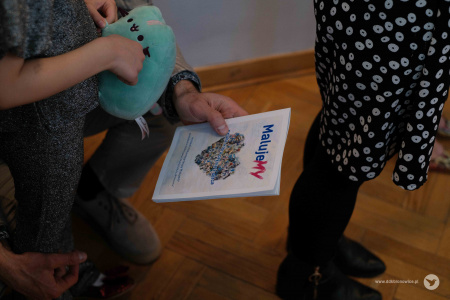 Mężczyzna trzyma w ręku folder dotyczący wystawy. Obok niego stoi mała dziewczynka.