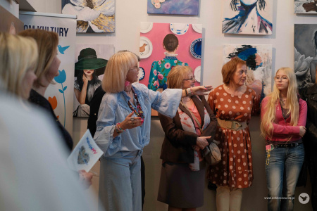 Przemówienie Moniki Szydłowskiej. Wskazuje na zawieszone obrazy i uczestników grupy MalujeMY.