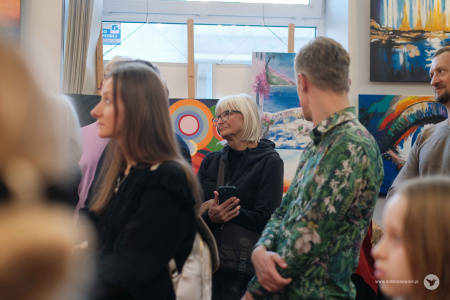 Mężczyzna w zielonej koszuli patrzy się w kierunku zawieszonych obrazów.