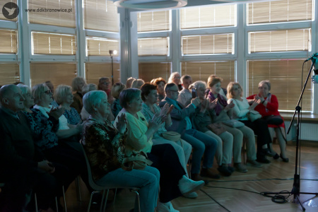 Widownia klaszcze w dłonie. W tle duże okna. Zaciągnięte rolety.