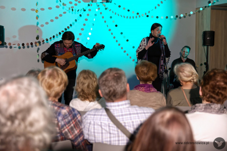 Na pierwszym planie widownia słuchająca w skupieniu koncert. W tle artyści.