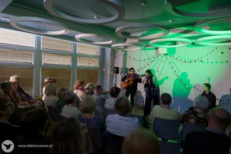 Trójka artystów grają piosenkę. W tle widać zielone światło. Na pierwszym planie siedząca widownia.