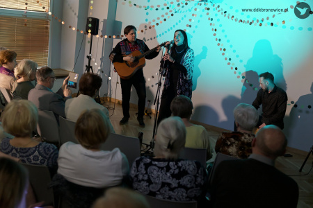 Artyści wykonują piosenkę. Oświetla ich błękitne światło. Na pierwszym planie siedząca i wsłuchana widownia.