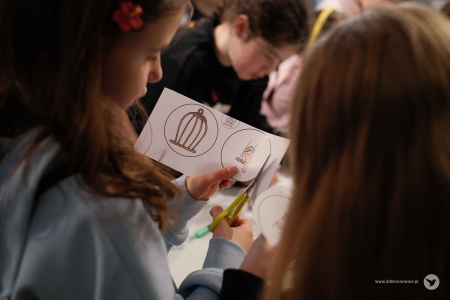 Dziewczynka w błękitnej bluzie wycina fragmenty papierowej ozdoby. W dwóch kółkach widać klatkę i ptaka.