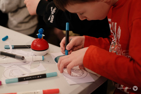 Chłopiec w czerwonej bluzie dokładnie koloruje papierową ozdobę.