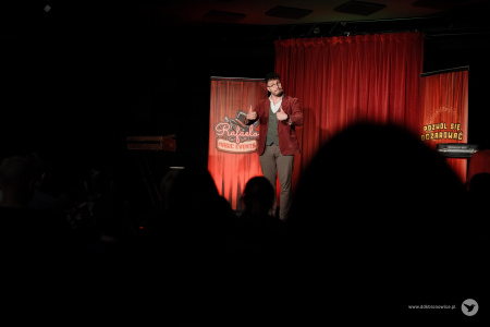 Magik na scenie pokazuje dwa kciuki w górze. Na pierwszym planie kontury osób na widowni.