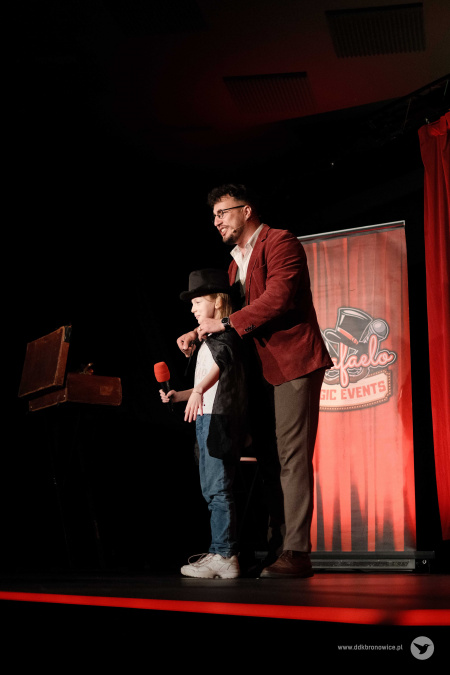 Magik zaprosił na scenę dziewczynkę. Zakłada jej czarną pelerynę i cylinder. Dziewczynka trzyma mikrofon.